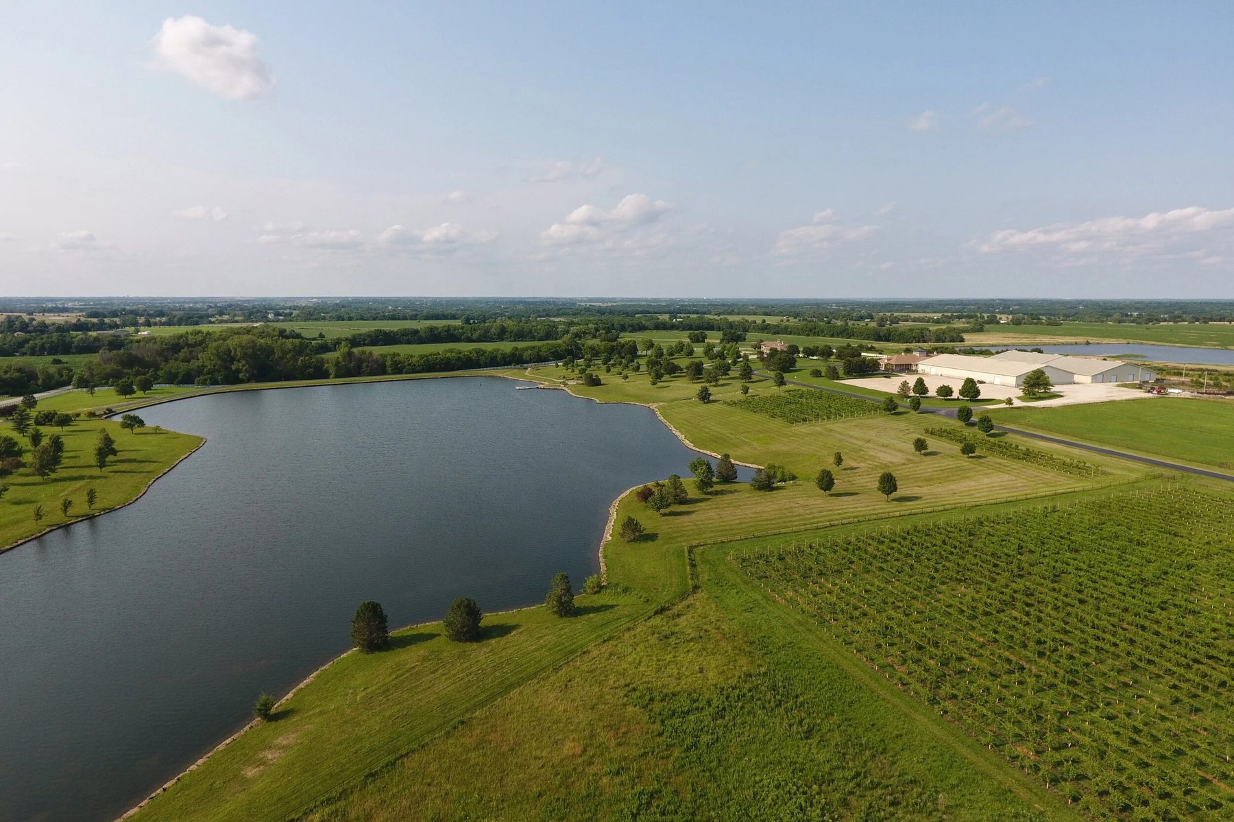 Aerial view of Bourgmont Winery: a large lake, rows of vines, and the event building beyond.